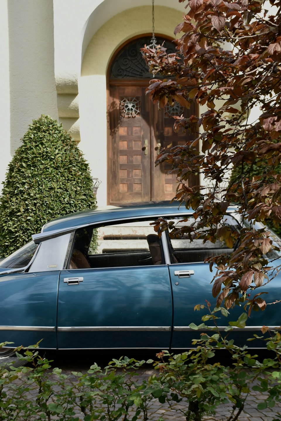 Classic blue car parked by stucco building with arched door.