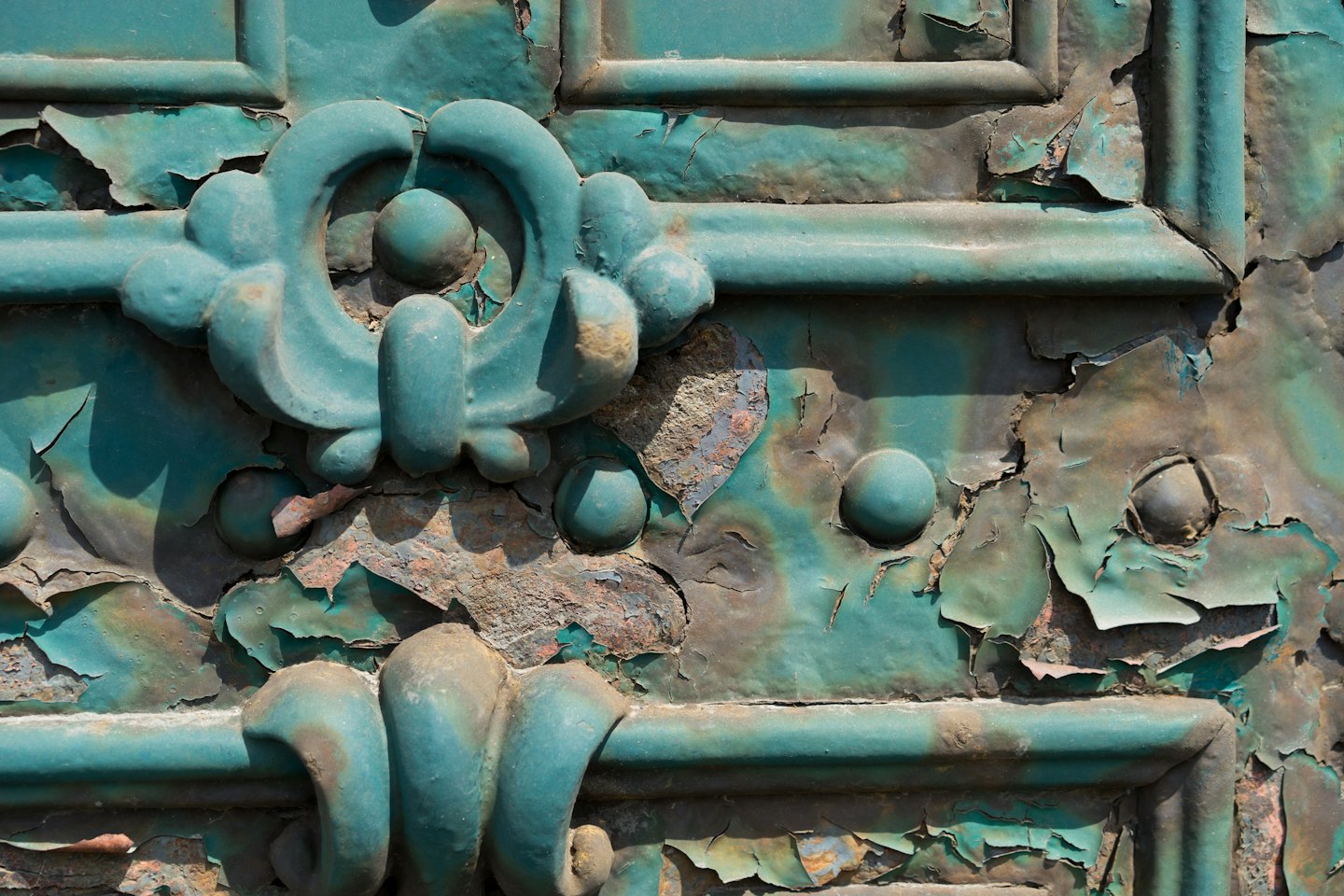 Peeling turquoise paint on weathered metal scrollwork.
