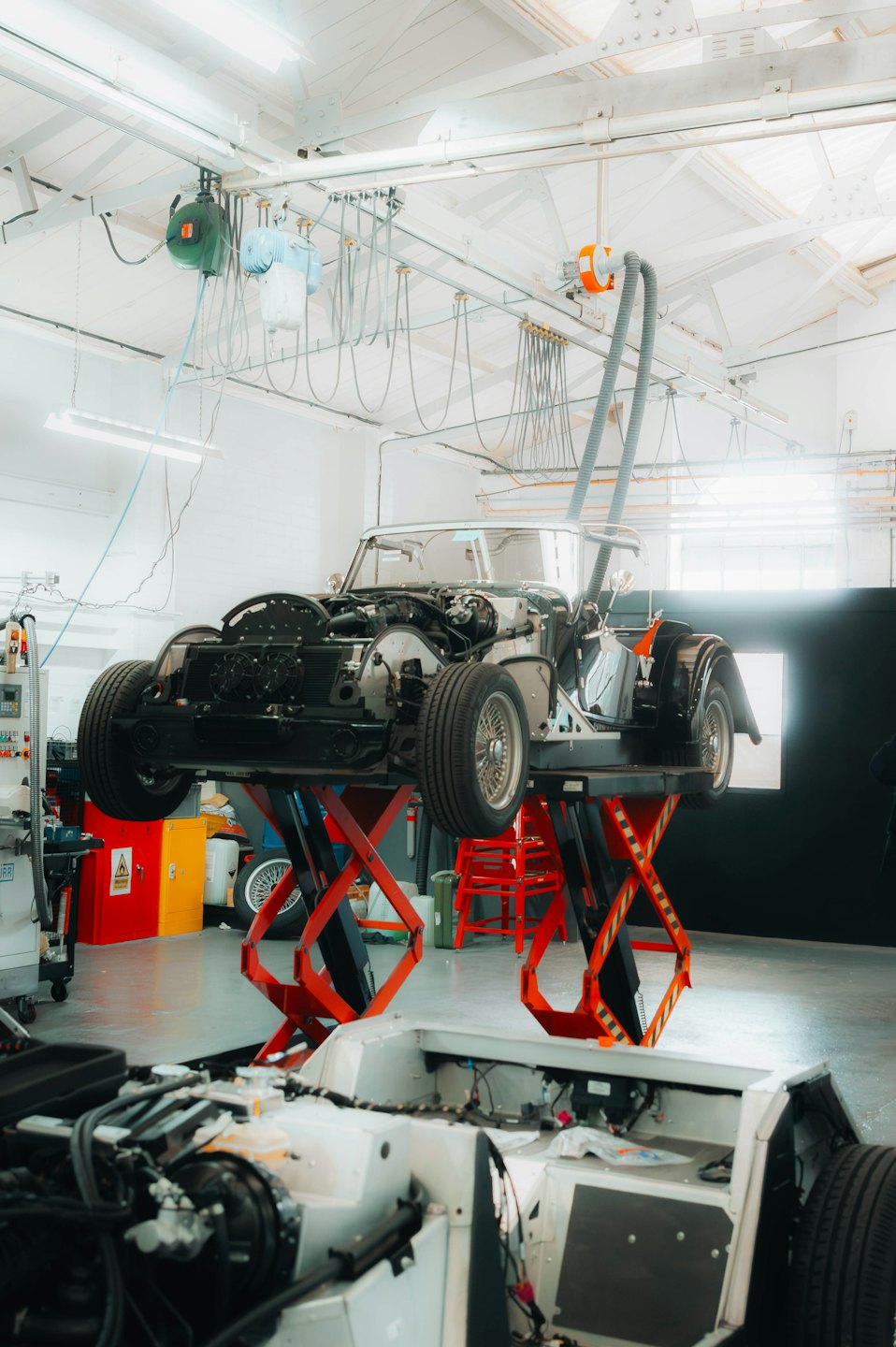 Classic car chassis on a red scissor lift in a workshop.