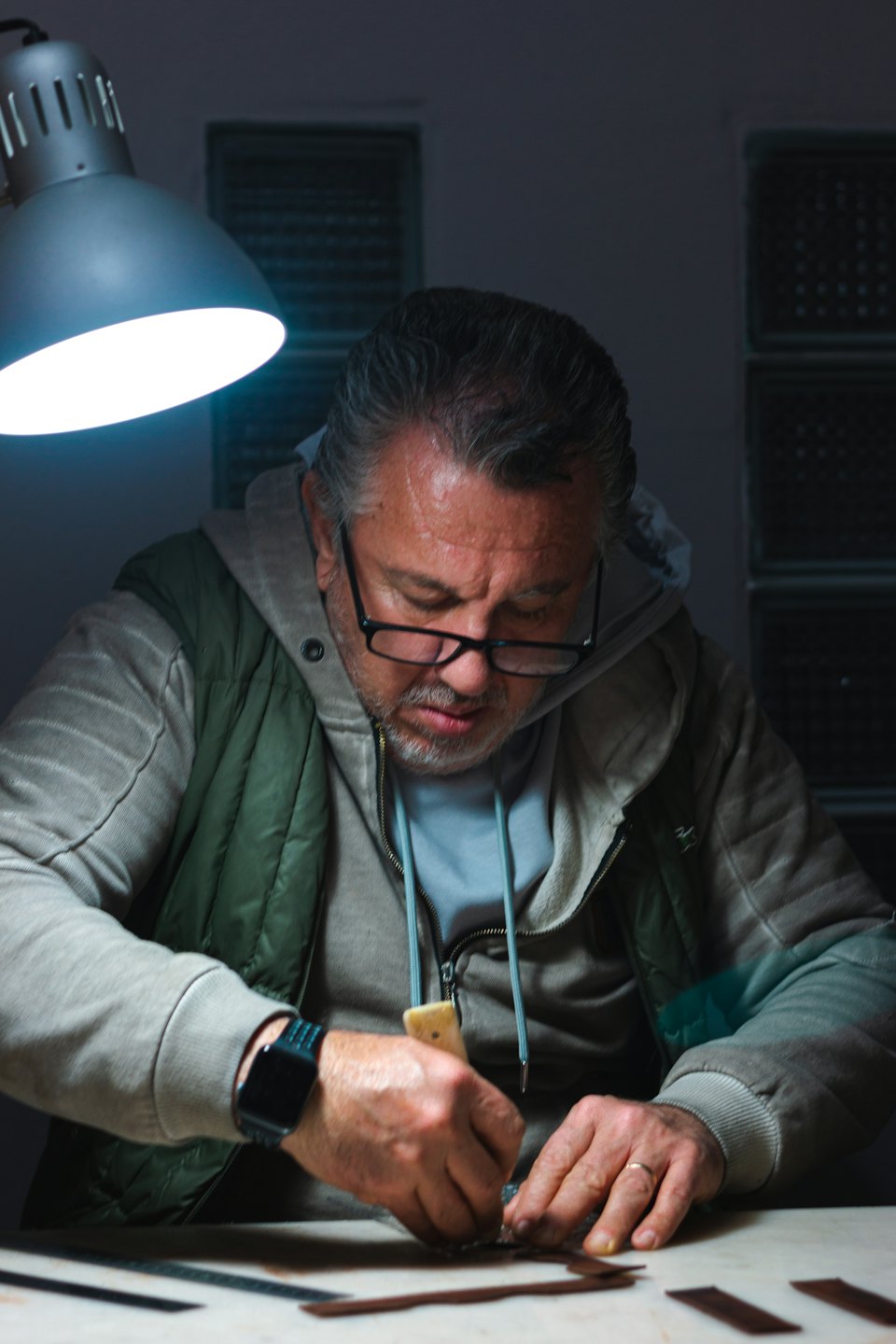 Craftsman with glasses meticulously working on leather with a tool.